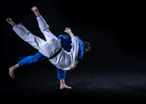 One in a blue gi executing a dynamic throw on an opponent in a white gi, against a black background.