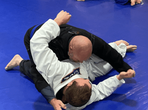 Two adults practicing Brazilian Jiu-Jitsu grappling techniques on a blue mat, showcasing adult Brazilian Jiu-Jitsu training.