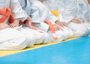 Young students in white gis and colored belts kneeling on a mat, training on their journey towards earning a judo black belt.