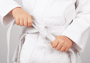 Child tying a judo belt represents the benefits of judo for building discipline and confidence.