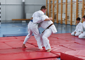 Two judo practitioners in white uniforms grappling on a red mat during training.