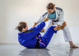 BJJ practitioners training, with one in open guard position and the other standing, focusing on technique and balance.