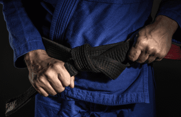 Close-up of a person in a blue gi tying a black belt, symbolizing dedication and progress in jiu-jitsu training.