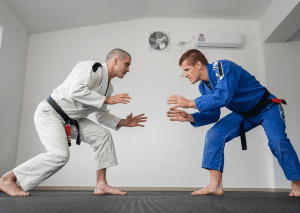 Two men in gis engage in jiu-jitsu training, demonstrating grappling stances on the mat.