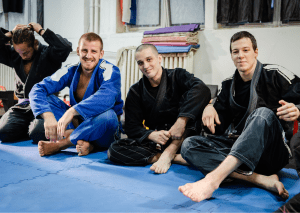 Group of jiu-jitsu practitioners in gis sitting on a mat, smiling and relaxing after training.