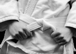 Close-up of a jiu-jitsu student in a white gi tightening their belt, symbolizing preparation and focus before training.