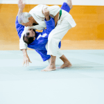 Two judo practitioners demonstrated judo takedowns on the mat, with one performing a throw on the other during training.