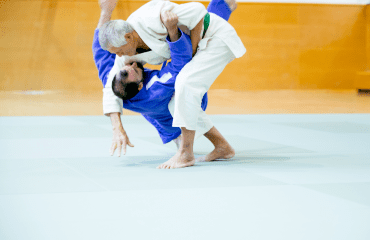 Two judo practitioners demonstrated judo takedowns on the mat, with one performing a throw on the other during training.