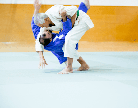 Two judo practitioners demonstrated judo takedowns on the mat, with one performing a throw on the other during training.