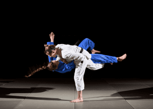 Two women in judo gi performing a dynamic throw during training, with a focus on technique and precision under spotlights.