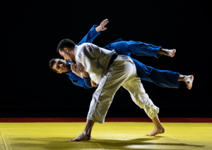 Two judokas execute a precise throw on a yellow mat with a black background, demonstrating the skill and balance of judo.