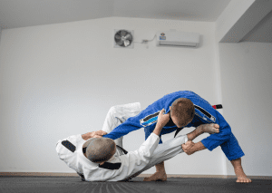 Two judo practitioners in gis grappling on the mat, demonstrating a guard pass technique during training.