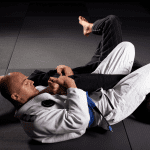 Two men practicing Brazilian jiu-jitsu on the mat, with one applying an armbar submission on the other.