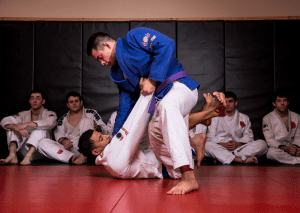 Brazilian jiu-jitsu training with a practitioner in blue gi applying guard pass technique as others observe.