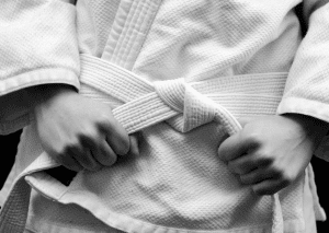 Close-up of a Brazilian jiu-jitsu student tightening their white belt, symbolizing discipline and dedication.