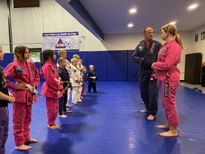 Kids in a jiu-jitsu class at Northern Colorado Jiu Jitsu listening to instructors, dressed in colorful uniforms.