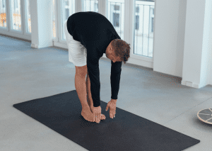 Man performing a forward fold stretch on a yoga mat, highlighting effective stretches for jiu-jitsu flexibility.