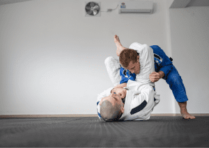 Two athletes practice adult jiu-jitsu fundamentals, one applying a submission hold on the other in a gym setting.